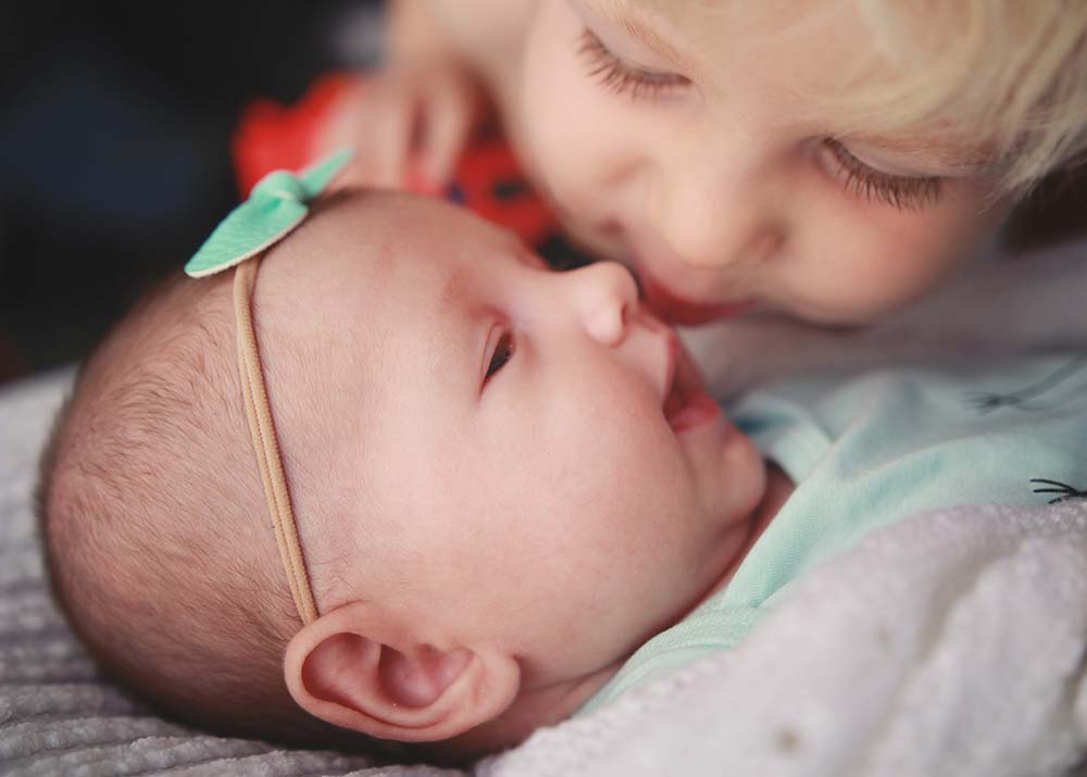 big-brother-giving-kisses-to-new-baby-sister-with-blaze-truck-Newborn-Photography-Lifestyle-Photographer