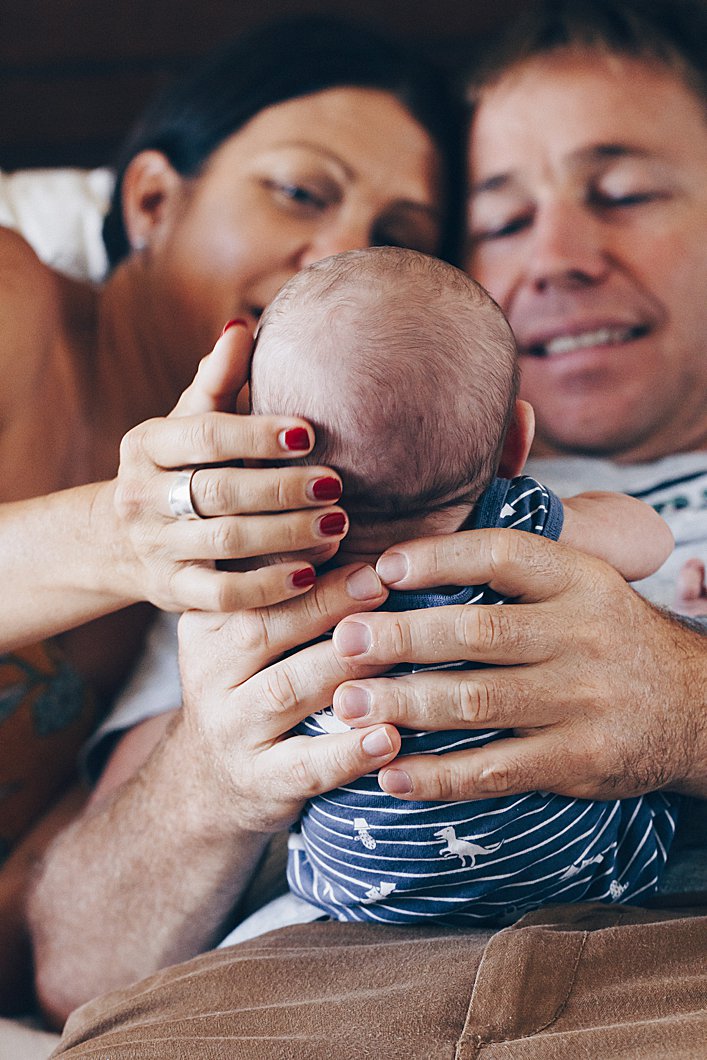 In-Home-Newborn-photography-session-parents-laying-on-bed-holding-newborn-son-and-just looking-at-him-in-love-with-their-hands-cradling-his-head-and-body-gold-coast-australia