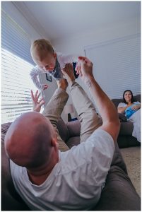 toddler-playing-with-dad-on-the-couch-being-lifted-into-the-air-from-dads-feet-newborn-inhome-photography-gold-coast