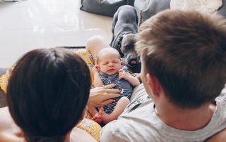 Newborn-son-having-a-little-squirm-in-mum-and-dads-lap-whilst-family-dog-sniffs-and-licks-his-lips