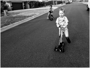two-kids-riding-a-bike-and-a-scooter-with-concentration-toungue-gold-coast-family-documentary-photography