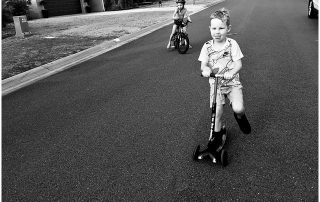 two-kids-riding-a-bike-and-a-scooter-with-concentration-toungue-gold-coast-family-documentary-photography