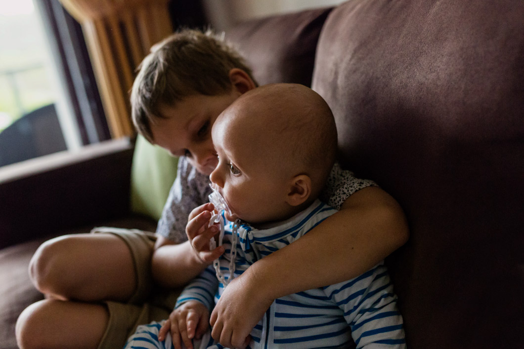 little-boy-giving-his baby-cousin-his-dummy-whilst-hanging-on-the-couch-together-as-part-of-a-holiday-family-documentary-photography-session-gold-coast