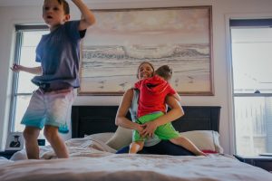 Two-kids-jumping-on-the-bed-with-mum-in-front-of-painting-that-was-their-grandmas-part-of-a-remembering-mum-series-gold-coast-australia-family-documentary-photography