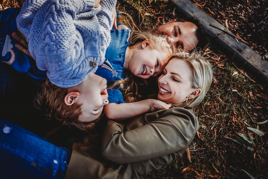 a-family-having-a-cuddle-puddle-on-the-ground-at-the-park,laughing-and-giggling-as-part-of-their-gold-coast-family-short-story-telling-photography-sessio