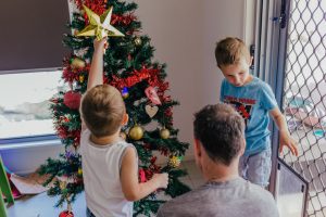 Young-boy-holding-up-the-xmas-tree-star-surrounded-by-his-dad-and-brother-as-they-work-to-decorate-the-tree