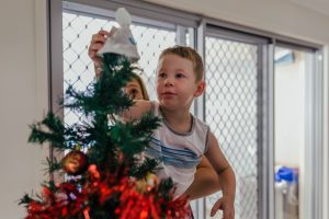 young-boy-crowning-the-xmas-tree-with-and-angel-being-lifted-up-by-mum