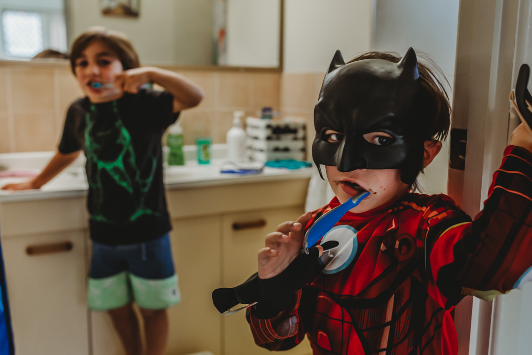 Super-hero-kids-watching-the-photographer-during-their-day-in-the-life-session-as-they-brus-their-teeth
