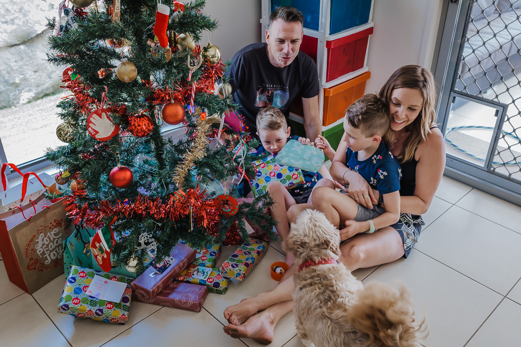 sweet family sitting by their Christmas tree having a cuddle with the kids as they excitedly look on over their Christmas tree