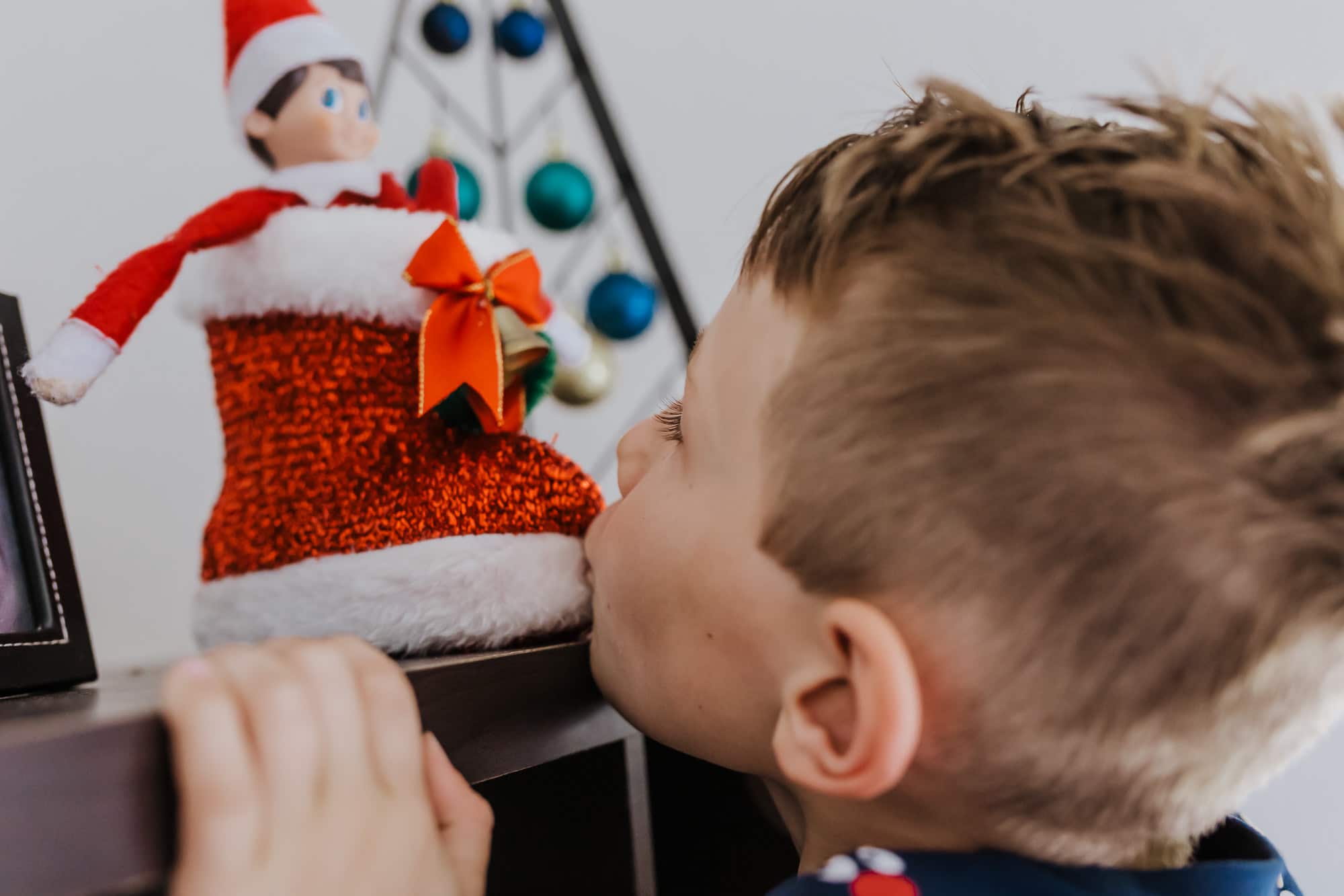 little 6 year old boy give the Elf on the Shelf a kiss on the big boot