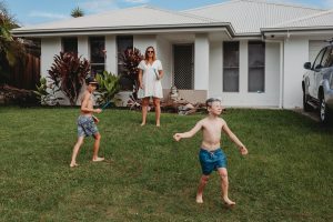 Mum playing with sons kicking the football in the front yard