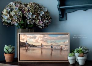 Room view of wood framed canvas of family on the beach spread out in a line, styled by vase of flowers and small plants